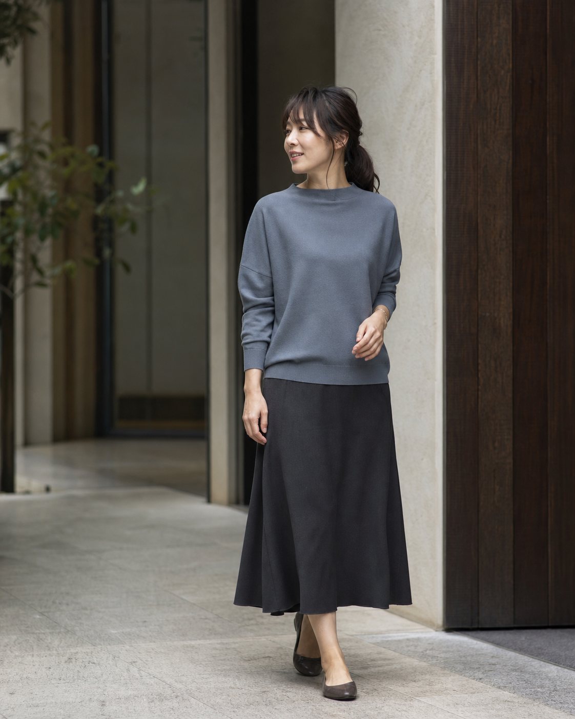 ブルーグレーのニットとチャコールのスカートを着た女性